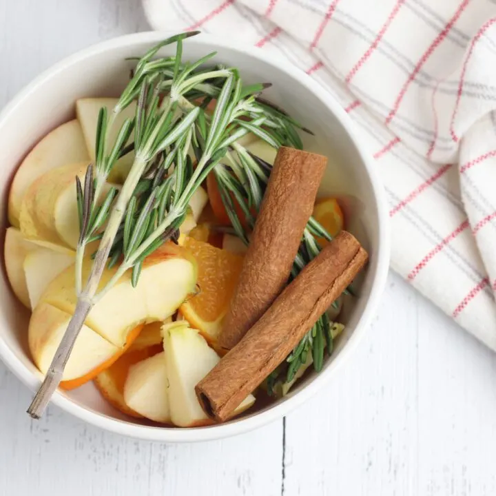 apples cinnamon sticks and rosemary in a white crock pot