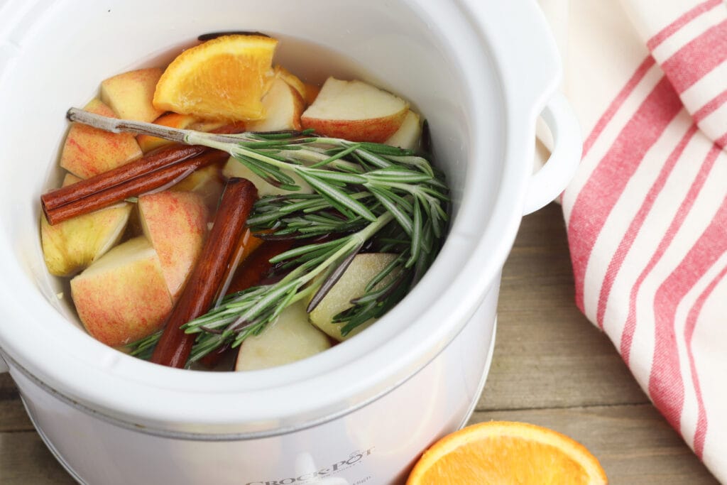 oranges apples cinnamon sticks and rosemary in a white crock pot for potpourri