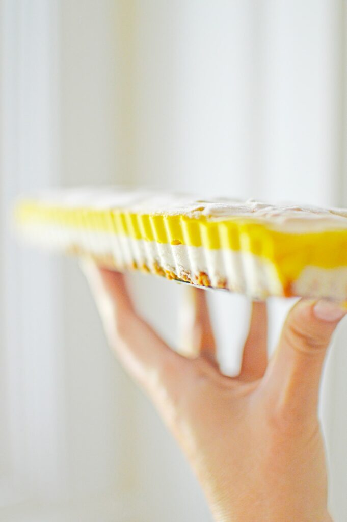 woman holding a layered pumpkin cheesecake bar on her fingertips against white background