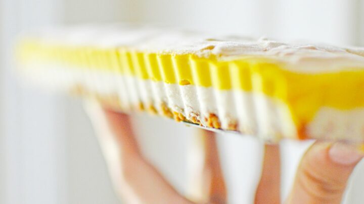 woman holding a layered pumpkin cheesecake bar on her fingertips against white background