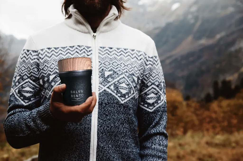 man holding a black insulated food jar while standing in the mountains