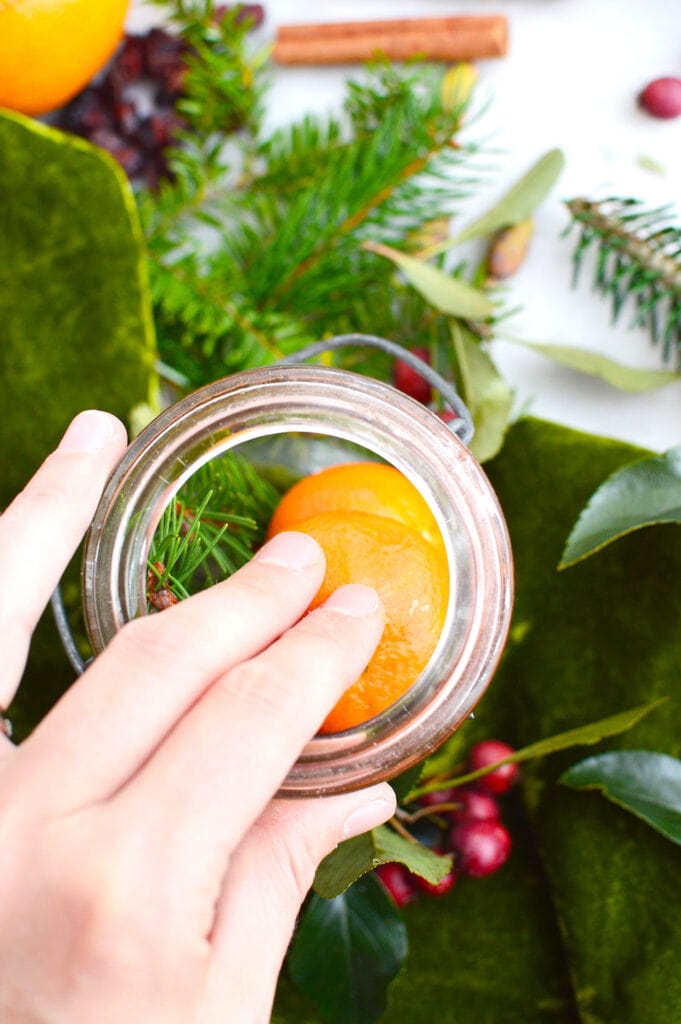 woman putting orange inside glass mason jar for potpourri