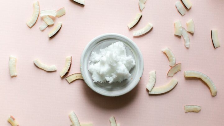 coconut oil in white bowl on pink background surrounded by coconut chips