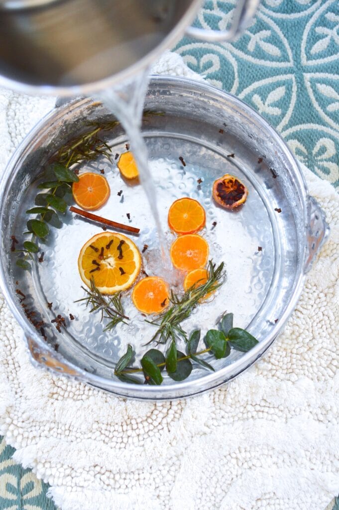 water pouring into silver pot filled with orange slices eucalyptus and cloves