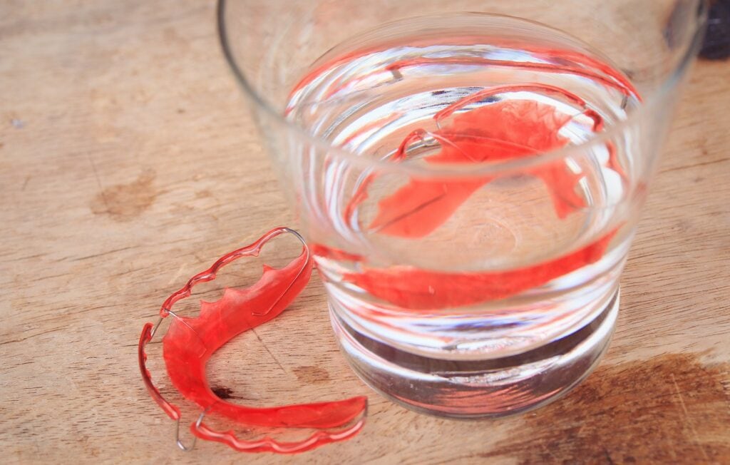 red retainer soaking in water and vinegar in glass on wood background