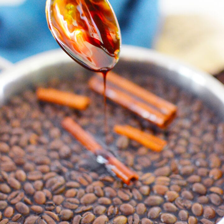 spoon with molasses dripping into coffee beans in pot with cinnamon sticks
