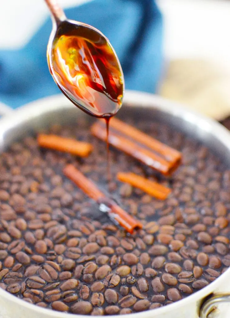 spoon with molasses dripping into coffee beans in pot with cinnamon sticks