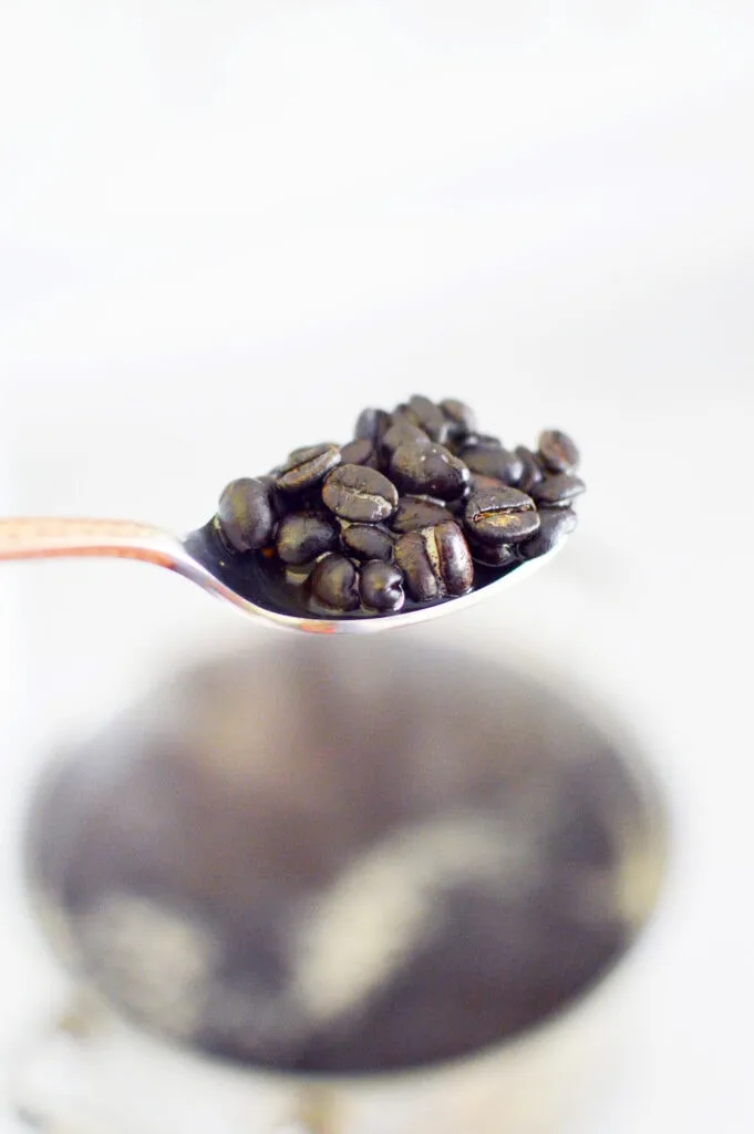 whole coffee beans on a silver spoon above a simmering pot