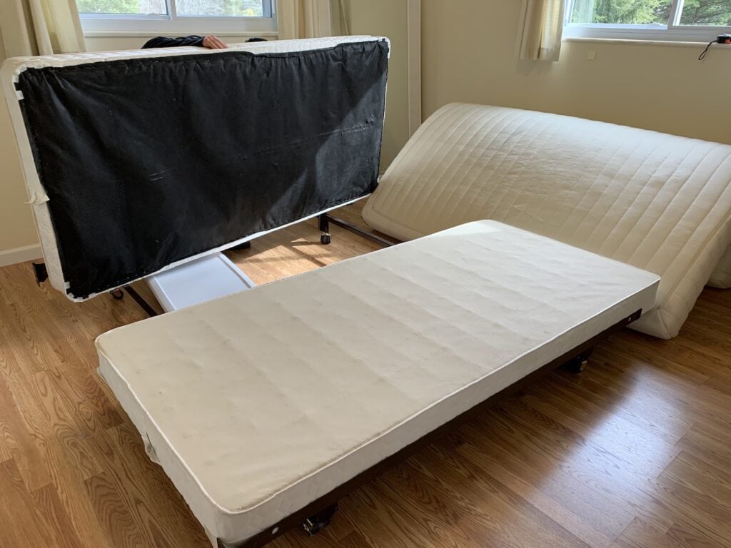 old box springs on metal bed frame with mattress in distance