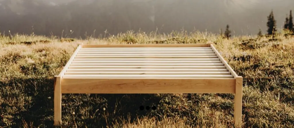 solid hardwood platform bed frame in grass with mountains in background