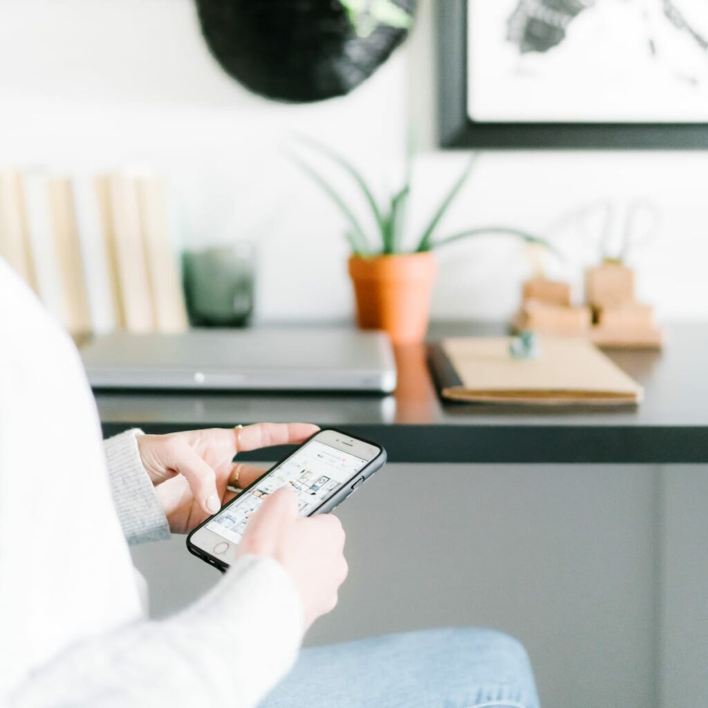 woman scrolling through social media on phone in home office