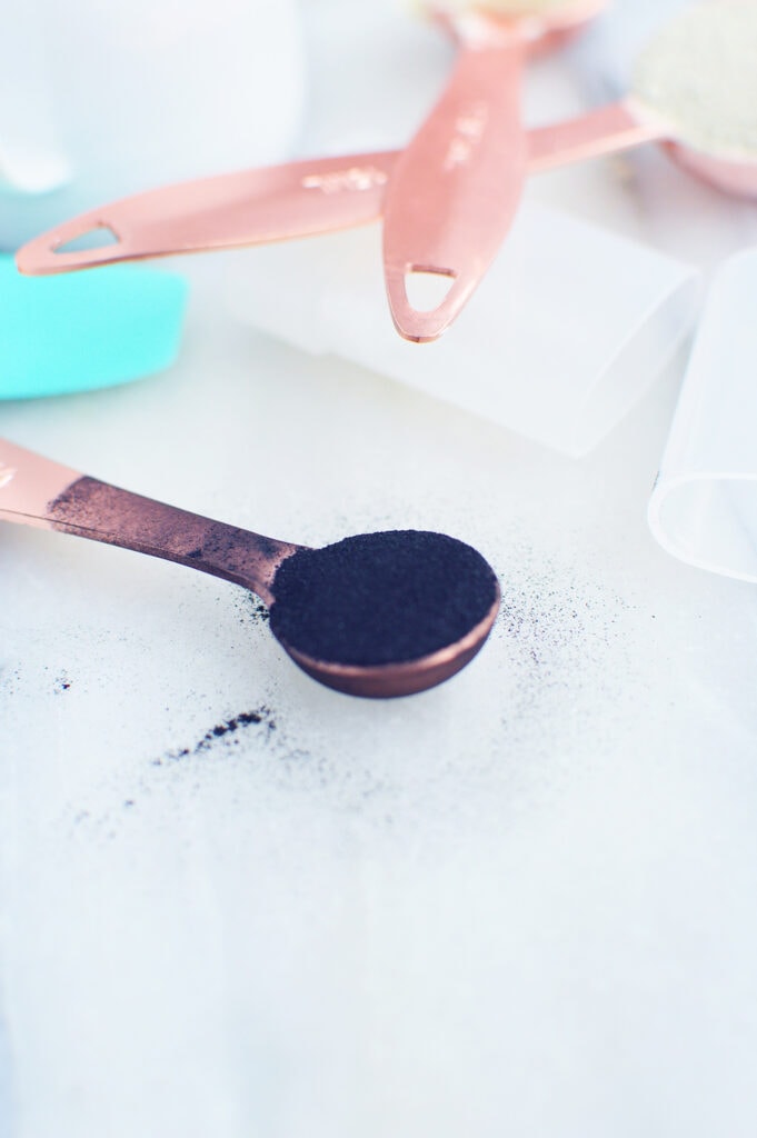 activated charcoal powder in copper measuring spoon on white surface