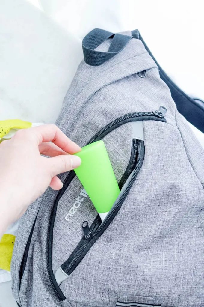 woman pulling out green bottle of diy hand sanitizer from grey backpack