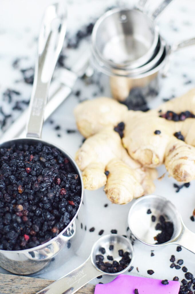 elderberries in stainless steel measuring cup on white background with large piece of ginger