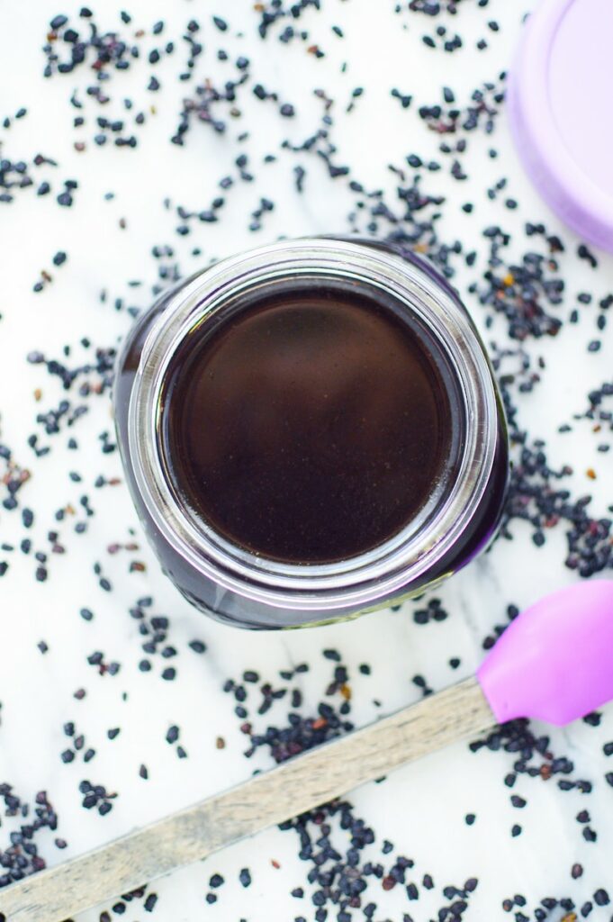 elderberry tonic for immune support in glass jar on white background surrounded by berries