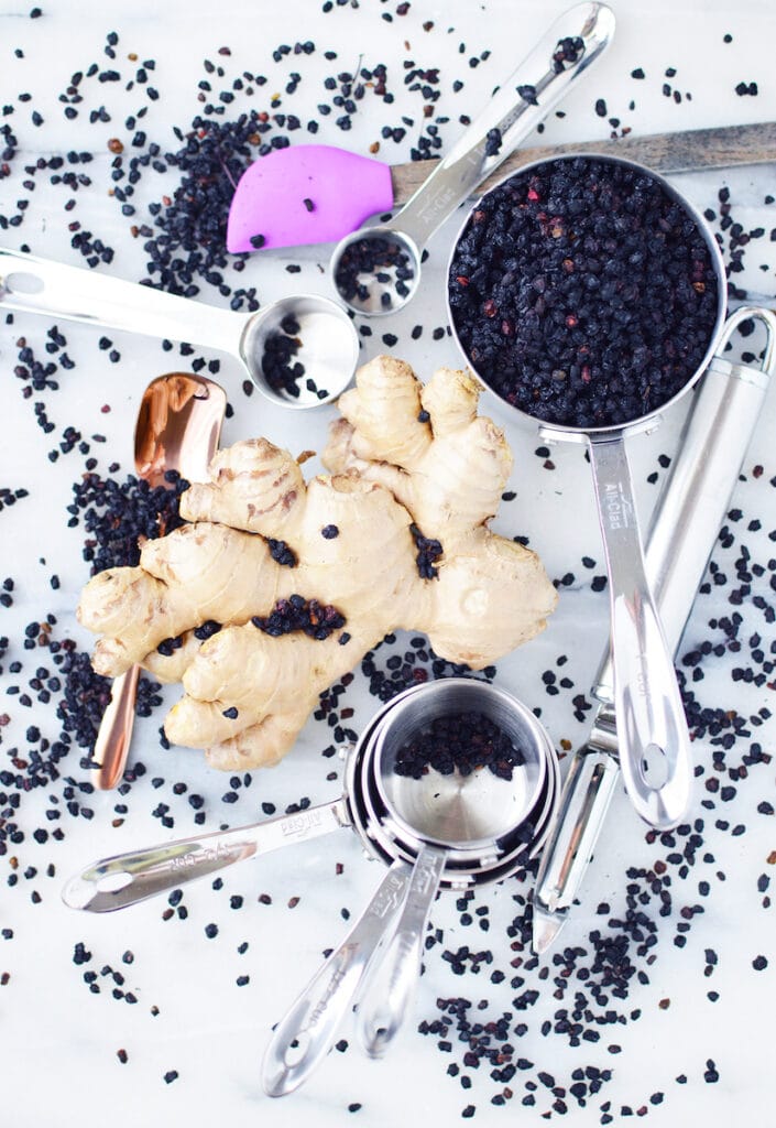 elderberries in measuring cup with large piece of ginger beside it