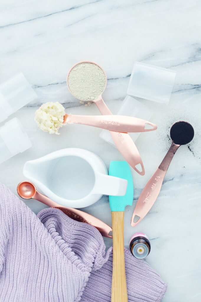 copper measuring spoons with charcoal shea butter and bentonite clay ingredients on white surface