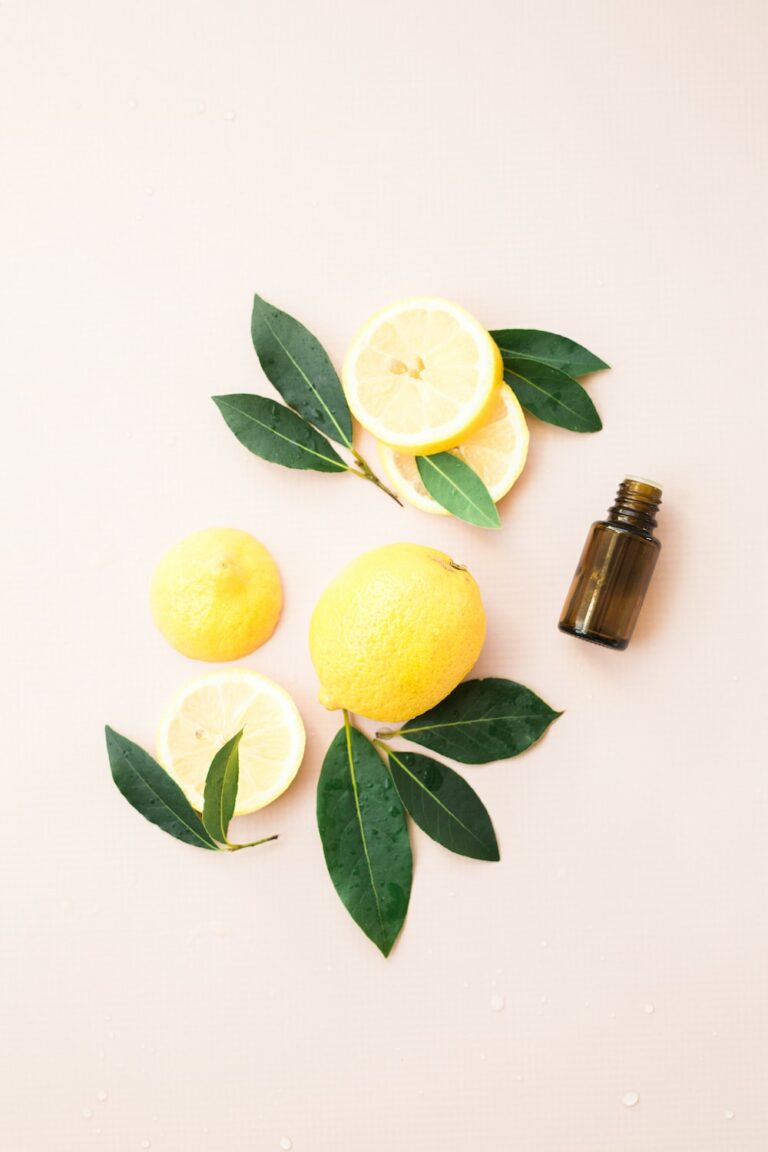 sliced lemons and leaves with brown essential oil bottle on pink background