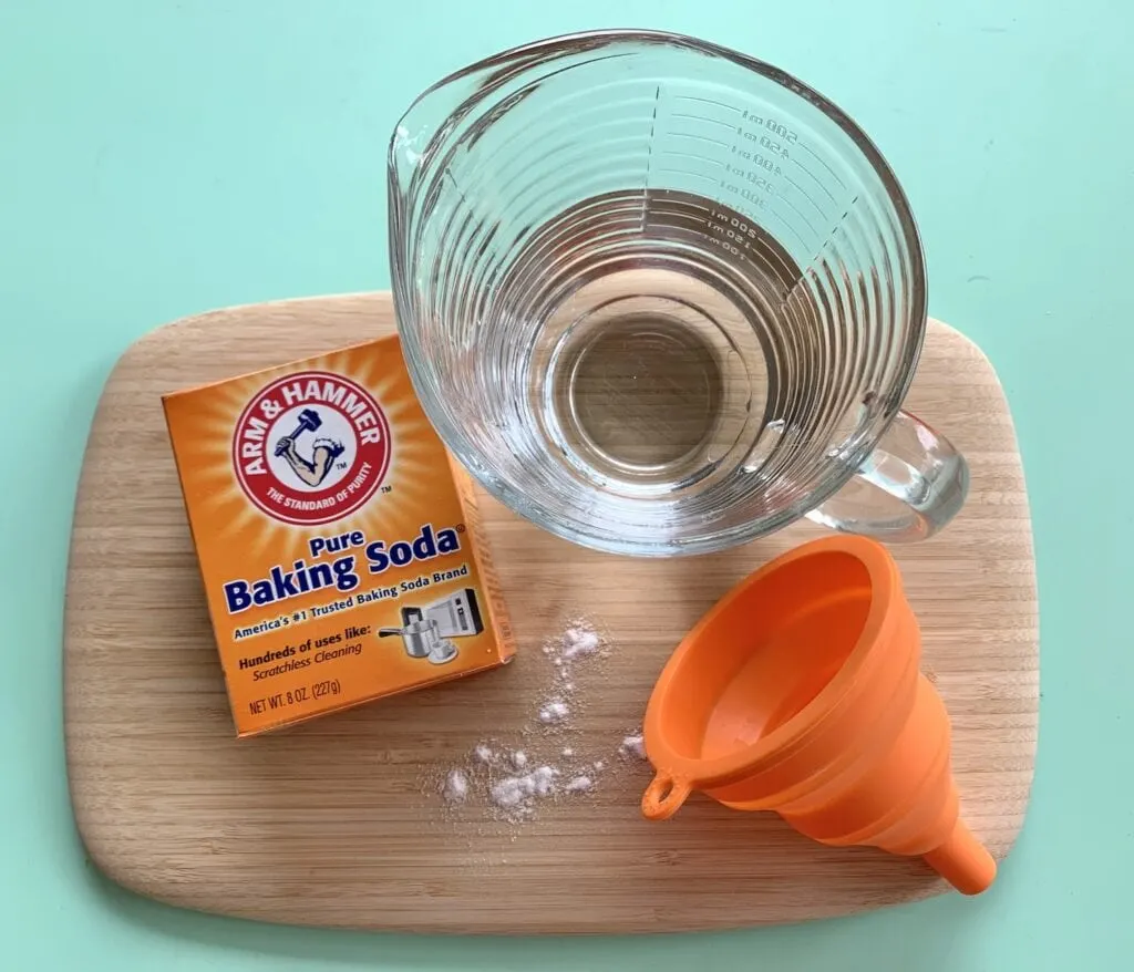 baking soda box funnel and glass measuring cup of water on wooden board against green table