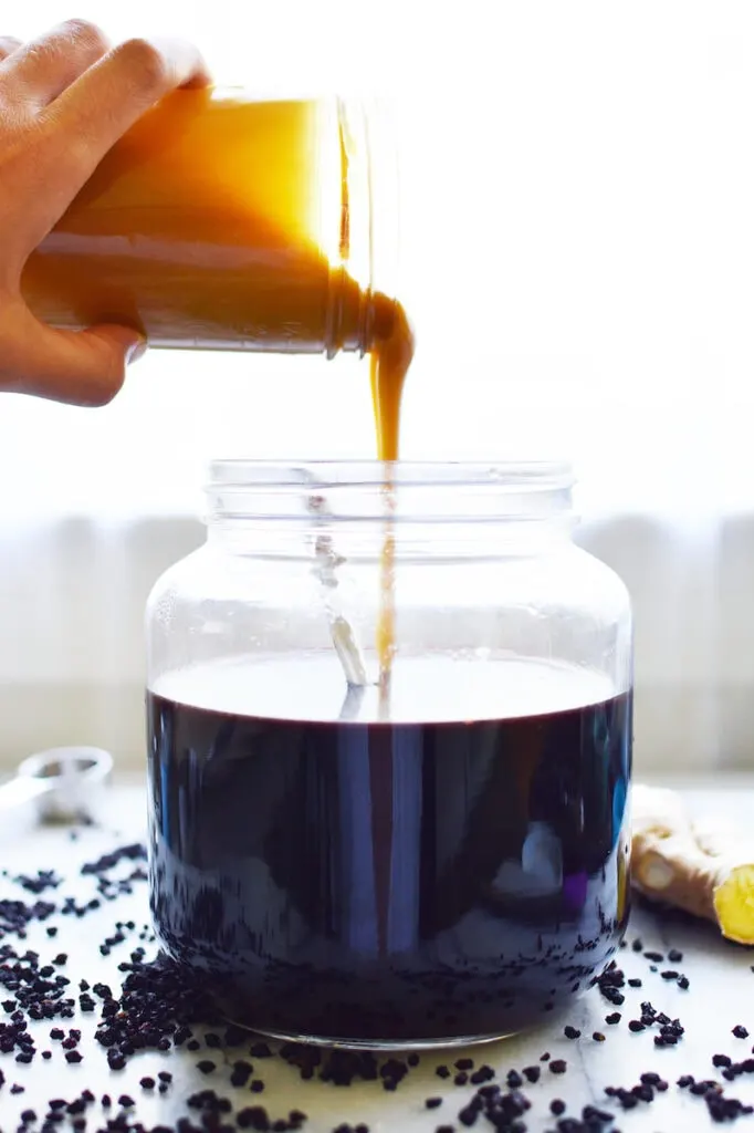 pouring honey into glass jar of elderberry tonic syrup