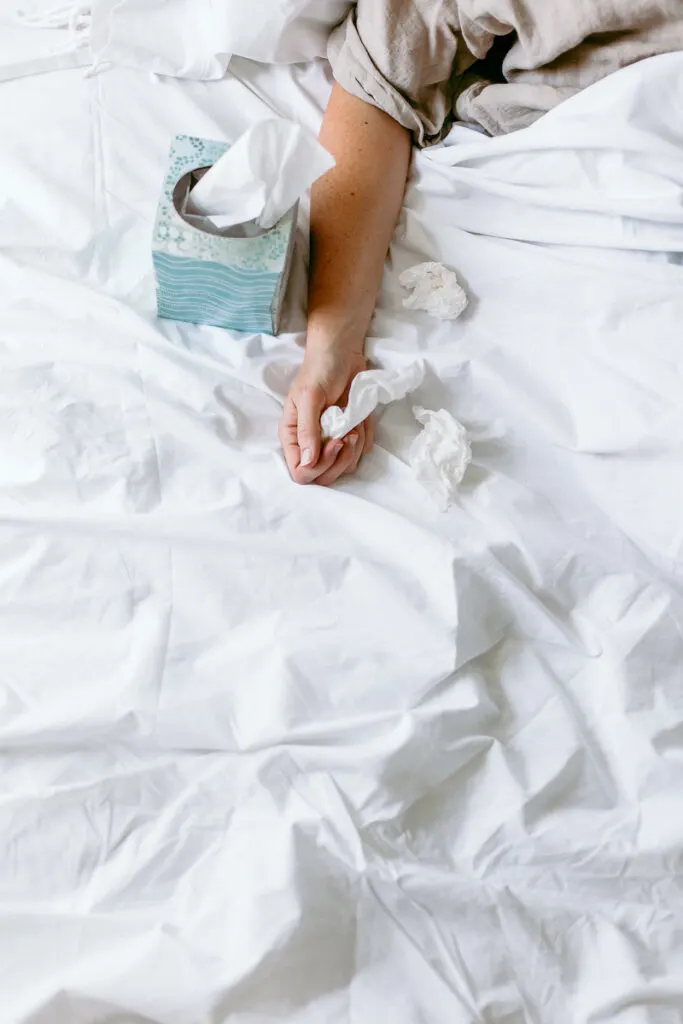 woman's hand holding bath tissues in bed with white sheets
