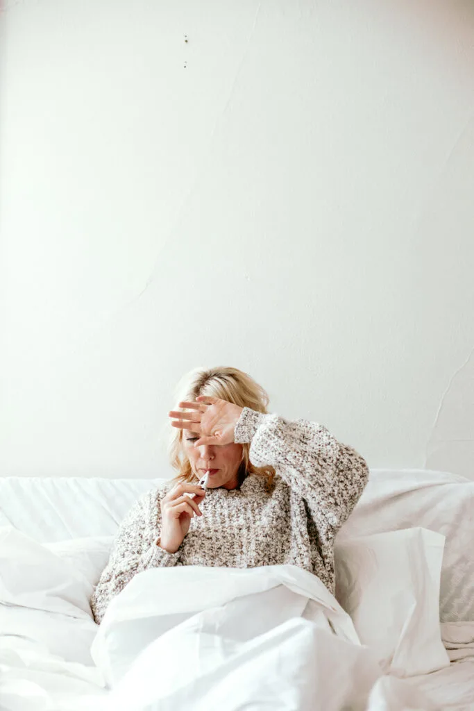 woman taking temperature in bed against white wall 