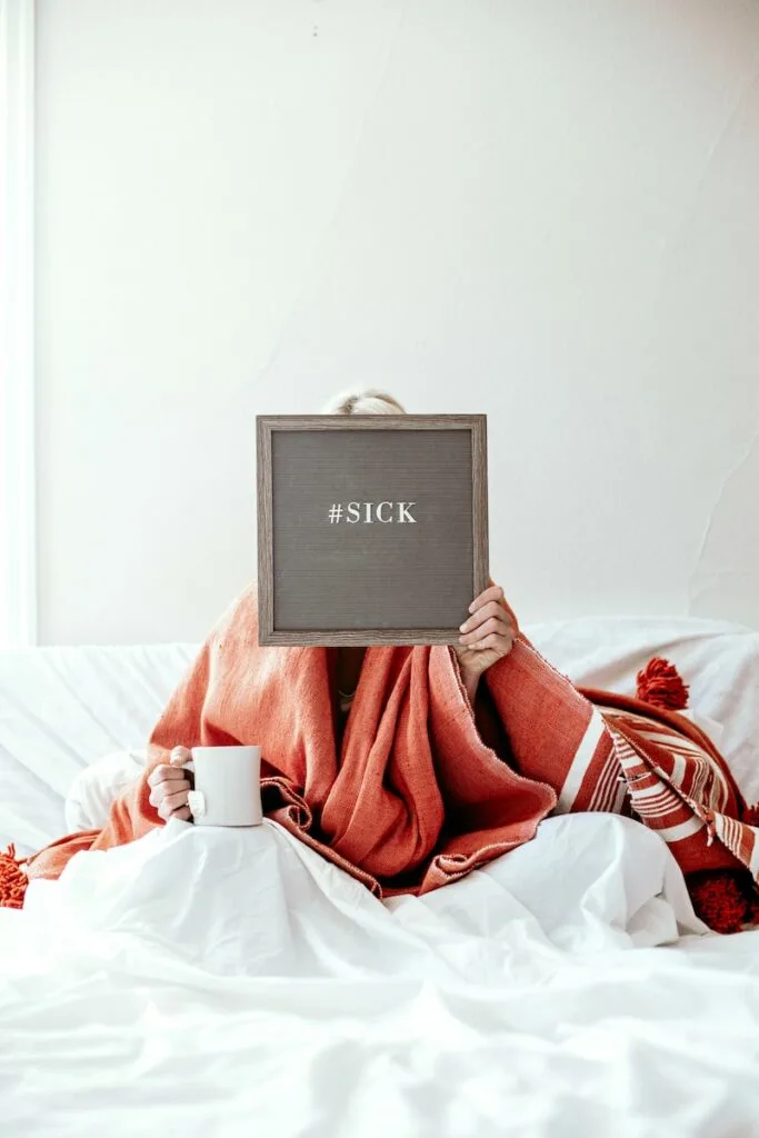 Woman holding up Board saying she is sick in Bed