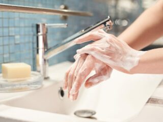 womans hands covered in soap at bathroom sink