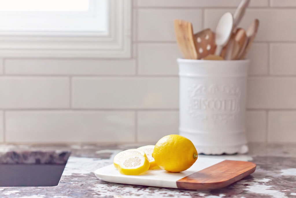 lemons on cutting board on marble countertop with kitchen gadgets in jar in background