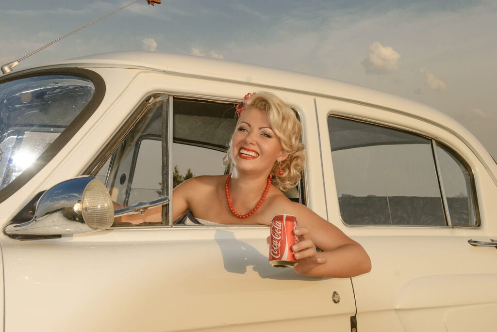 old fashioned woman sitting in retro car holding a can of Coca Cola