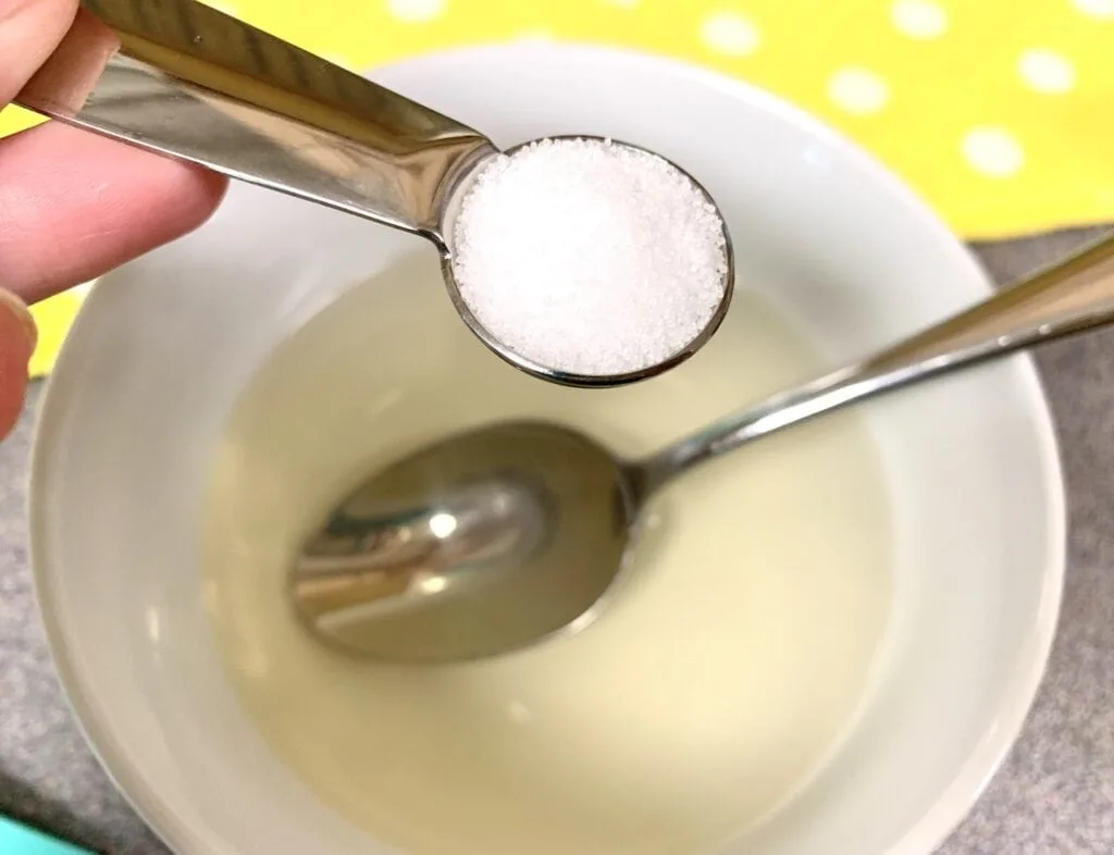 stainless steel teaspoon of table salt held over bowl of Jello