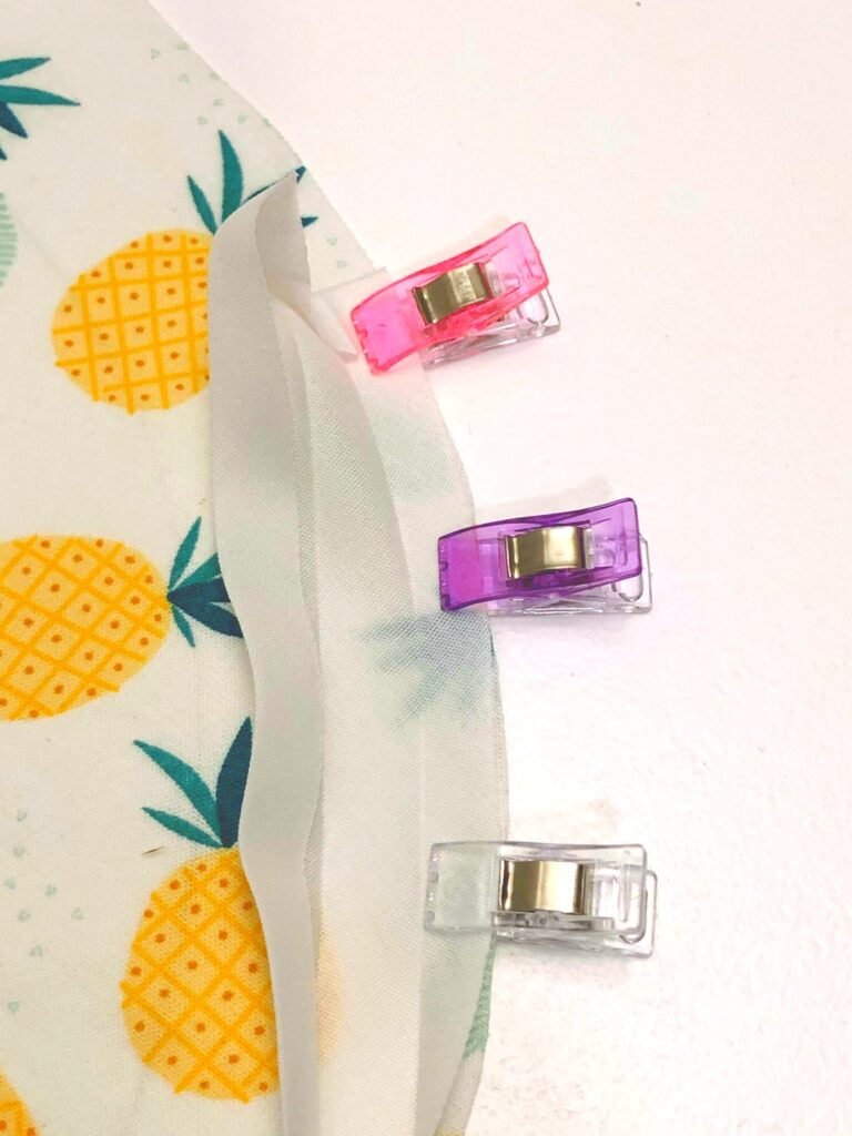 small plastic clips holding white bias tape to edge of circle of fabric