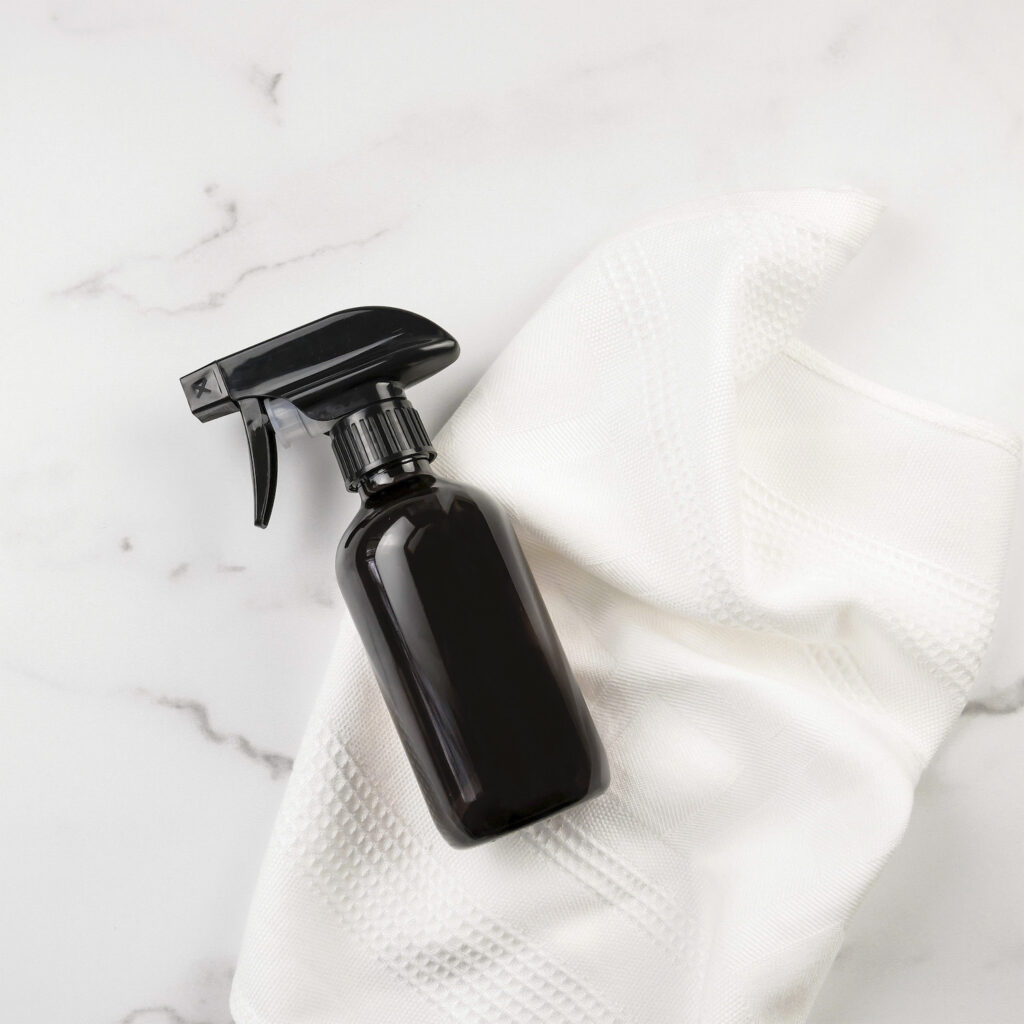 dark glass spray bottle on white towel against marble background