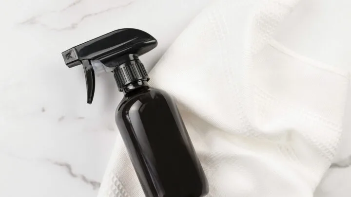 A black spray bottle and a white cloth, perfect as the best gifts for germaphobes, are placed on a marble surface.