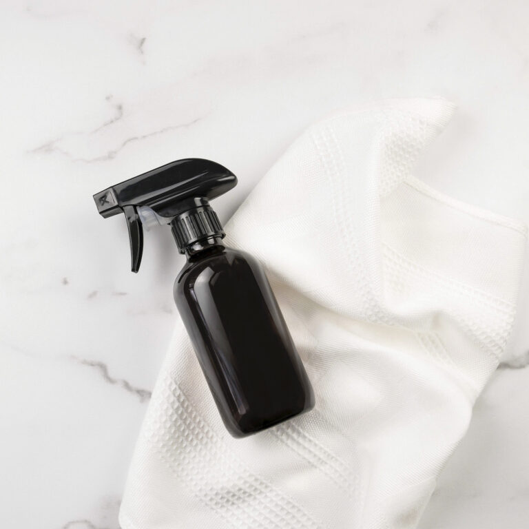 A black spray bottle and a white cloth, perfect as the best gifts for germaphobes, are placed on a marble surface.