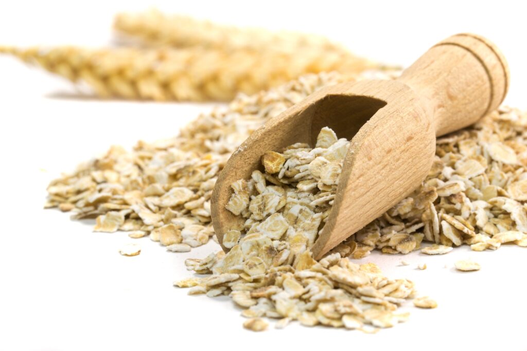 wooden spoon with oatmeal flakes against white background