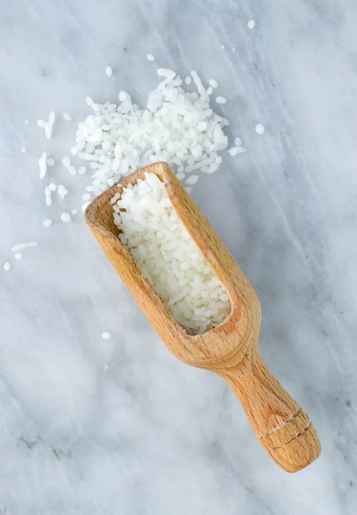 beeswax pellets in wooden scoop on marble background