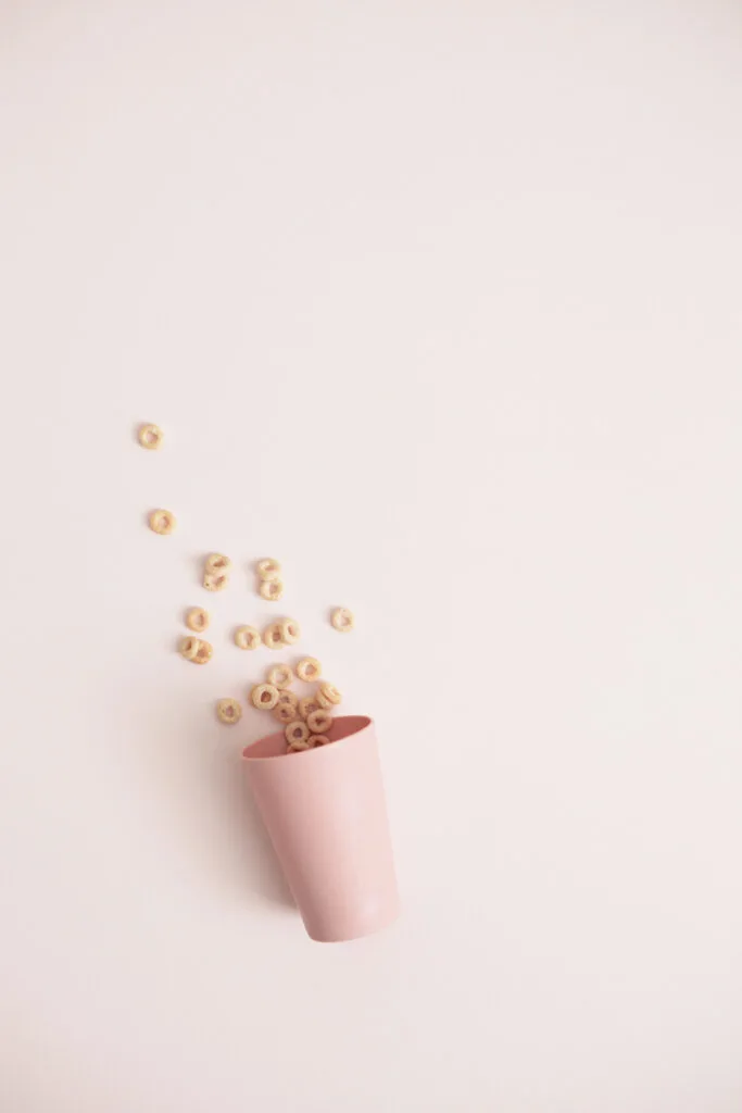 pink plastic cup with cheerios spilling out onto pink background