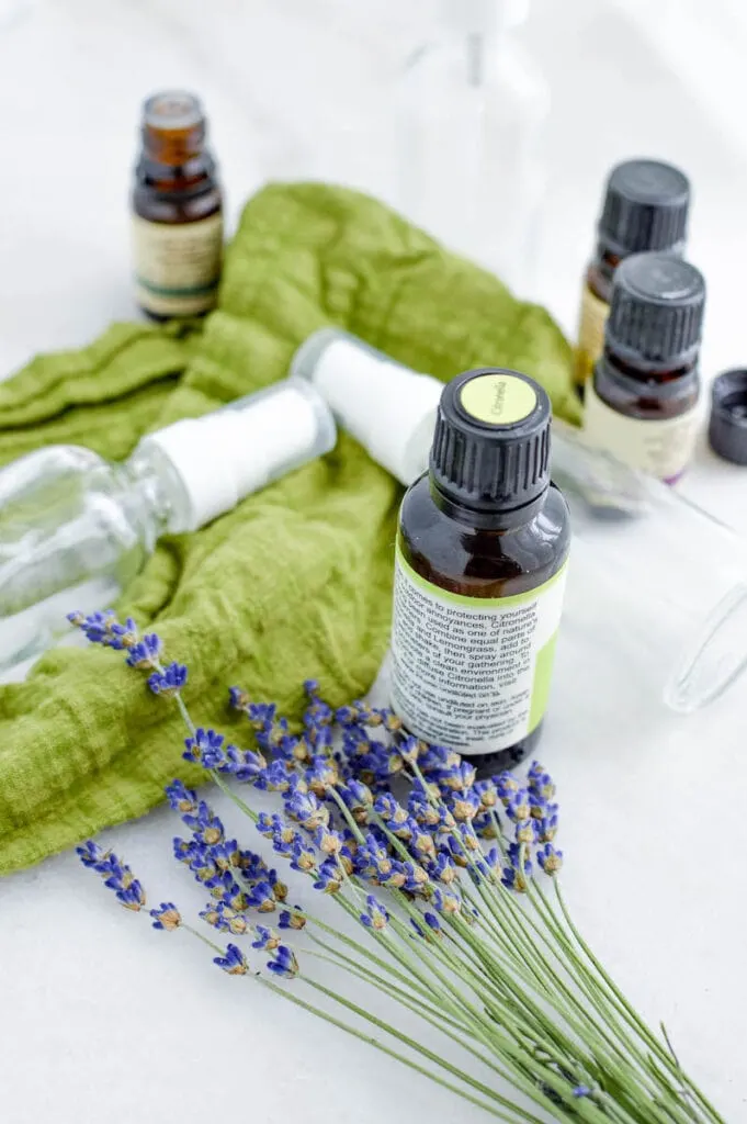 glass spray bottles with essential oils and lavender flowers on green fabric