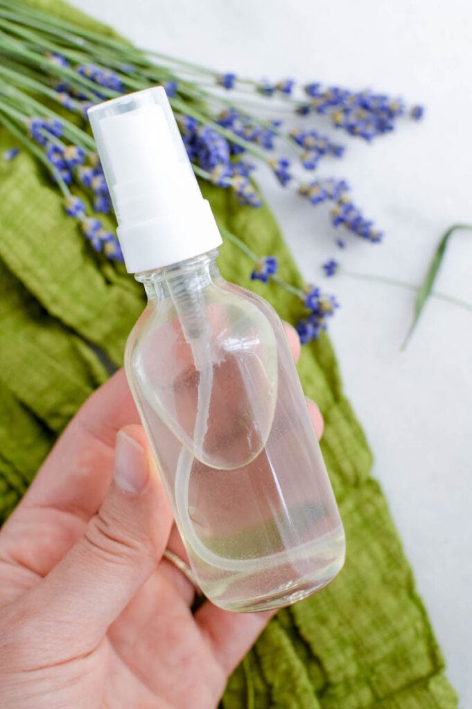 woman holding glass spray bottle with lavender plants in background