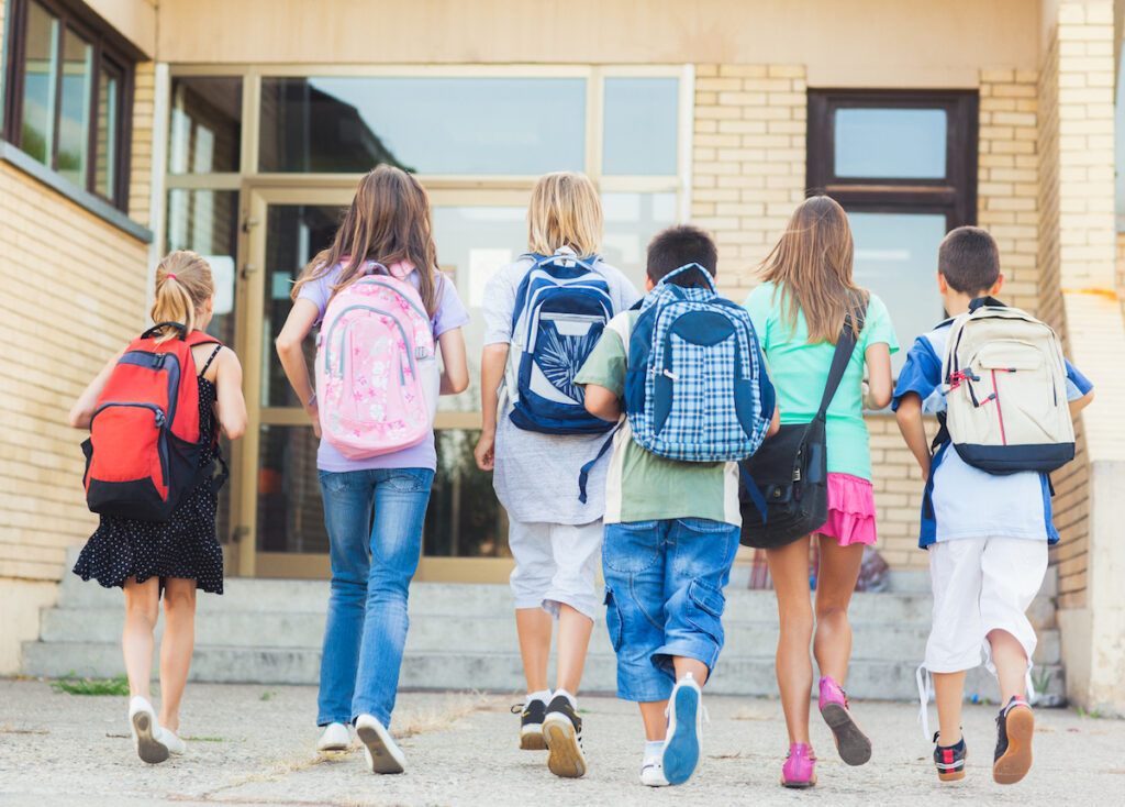 kids wearing backpacks walking towards school