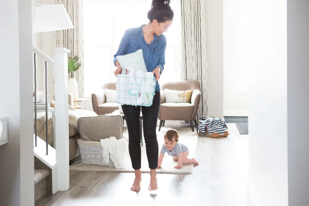 mom carrying laundry basket and baby crawling on floor