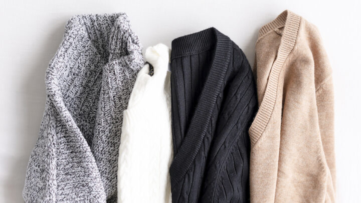 Four knitted sweaters in gray, white, black, and beige are laid out in a row on a white surface. Wondering how to get the smell out? These cozy essentials are as fresh as they look!