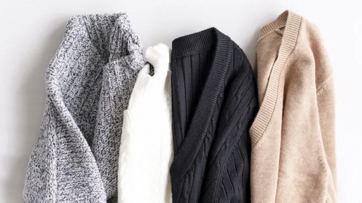 Four knitted sweaters in gray, white, black, and beige are laid out in a row on a white surface. Wondering how to get the smell out? These cozy essentials are as fresh as they look!