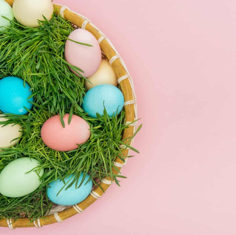 colorful Easter eggs in grass in basket with pink background