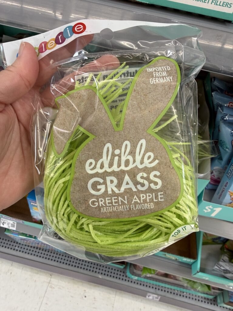 A hand holds a package of green apple flavored edible grass in front of a store shelf