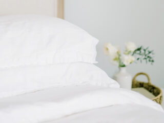 white sheets on a bed with flowers on a bedside table