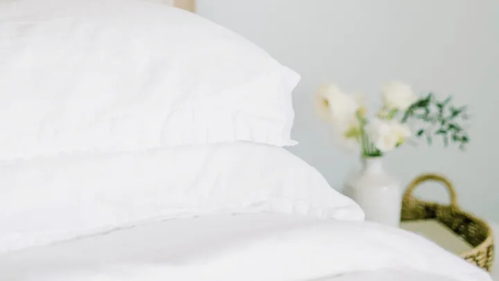 white sheets on a bed with flowers on a bedside table