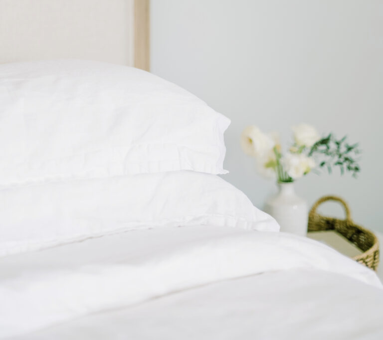 white sheets on a bed with flowers on a bedside table