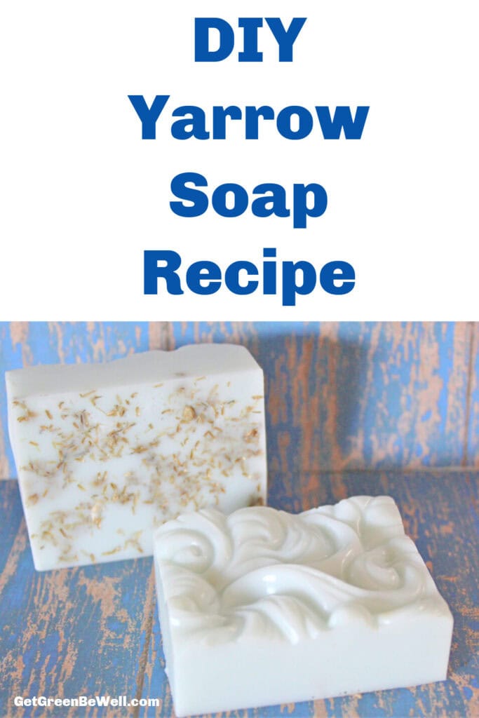 Two handmade yarrow soap bars, one with yarrow flowers embedded and the other featuring a decorative swirl pattern, are placed on a blue and wood-textured surface. Text above reads &ldquo;DIY Yarrow Soap Recipe.&rdquo;.